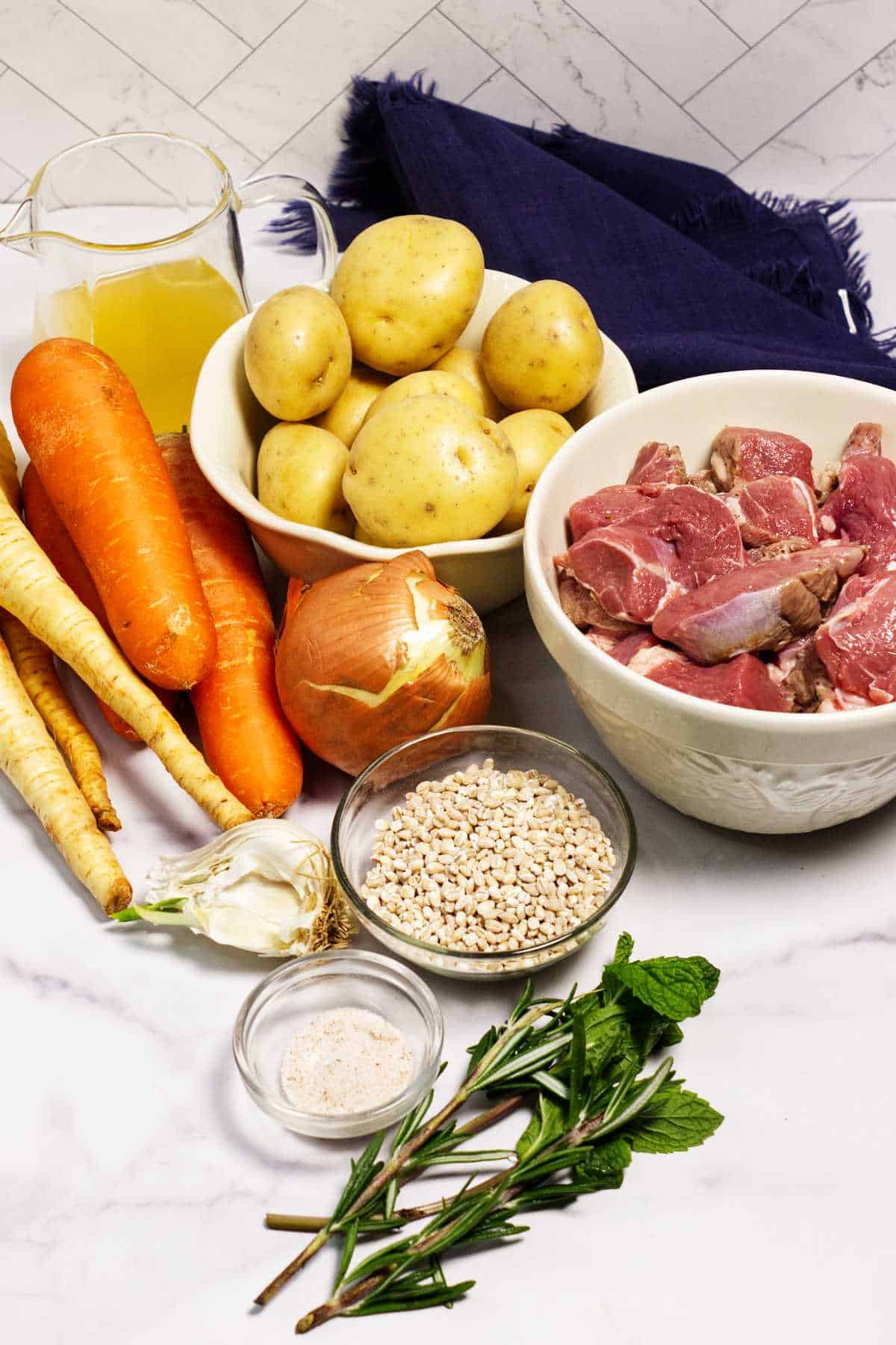 Ingredients for Irish lamb stew including lamb, potatoes, carrots, parsnips, barley, and herbs.