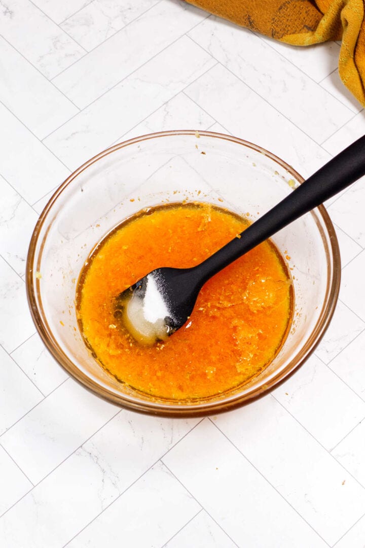 Sugar and toasted sesame oil added to the carrot ginger dressing mixture in a glass bowl.