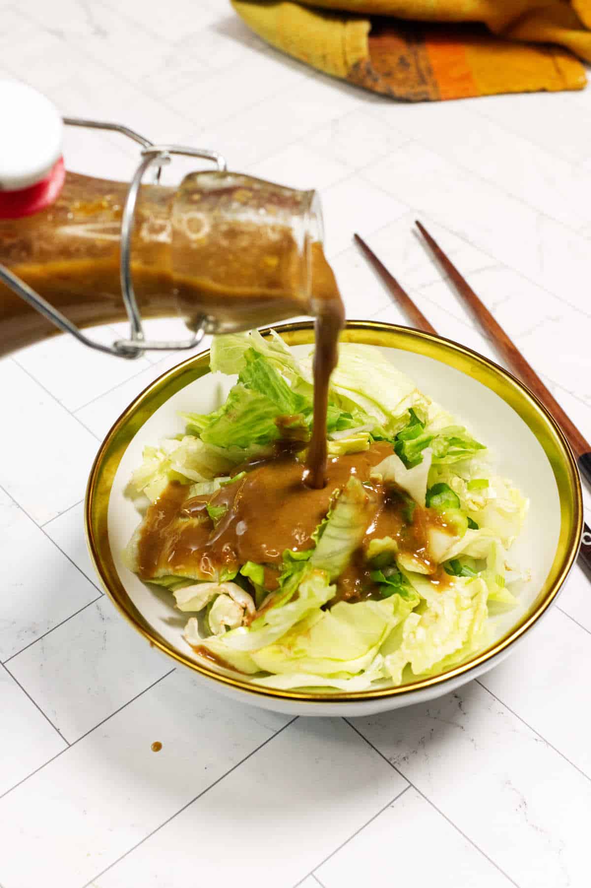 Japanese steakhouse carrot ginger dressing being poured over a bowl of chopped iceberg lettuce.