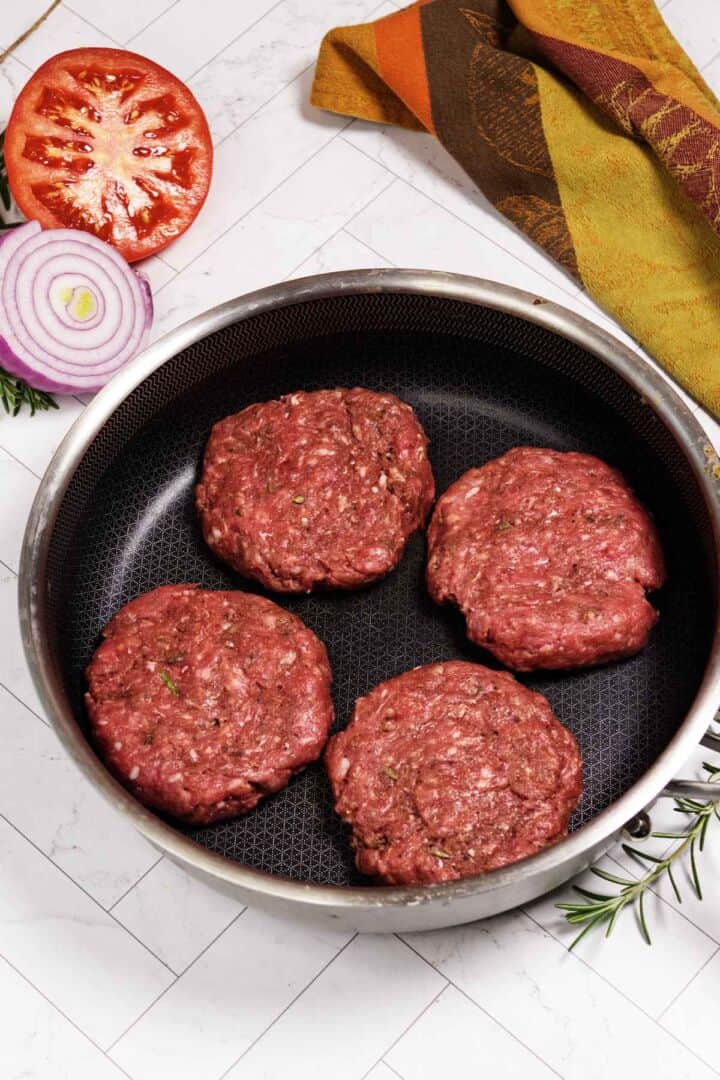 Raw lamb burger patties arranged in a cast iron skillet before cooking.