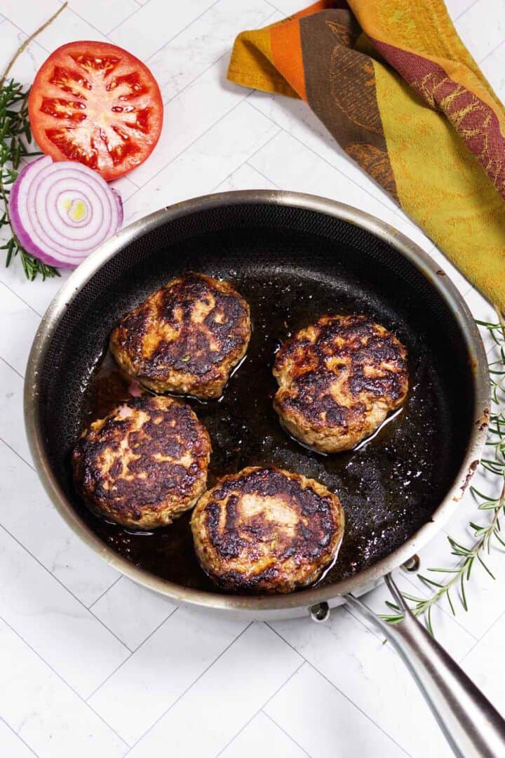 Lamb burger patties browning in a cast iron skillet.