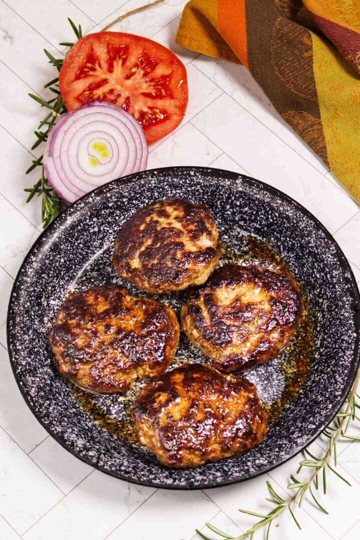 Cooked lamb burger patties on a platter with tomato and red onion nearby.