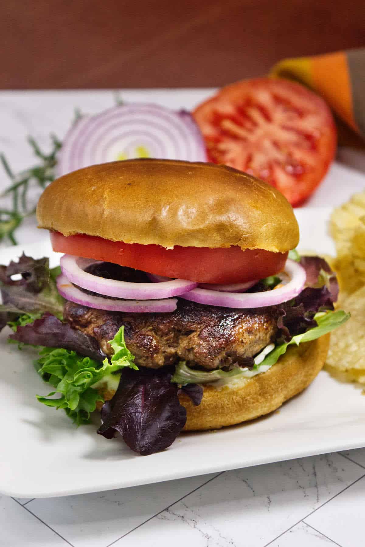 Lamb burger with arugula, tomato, red onion, and lettuce served with potato chips.