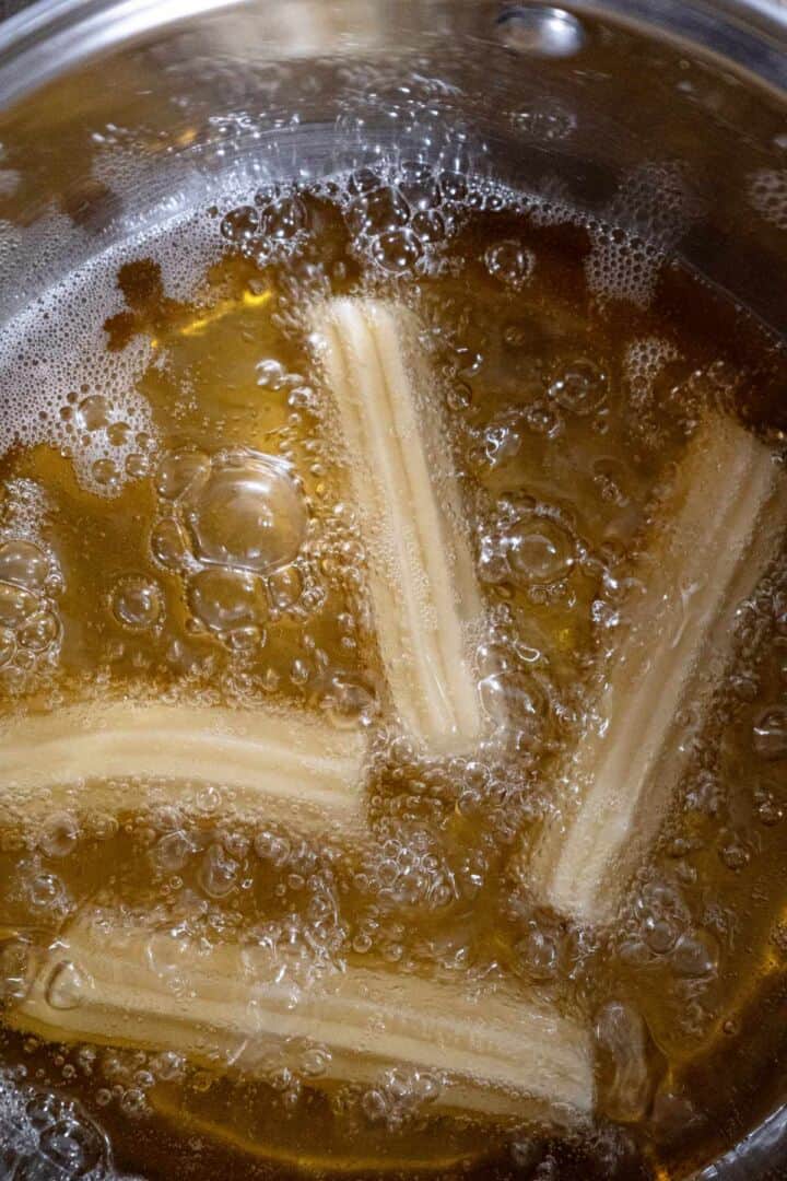 Churros frying in hot oil until golden brown.
