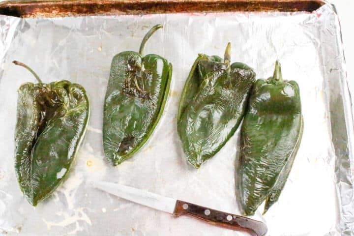 Roasted poblano peppers on a foil lined baking sheet.