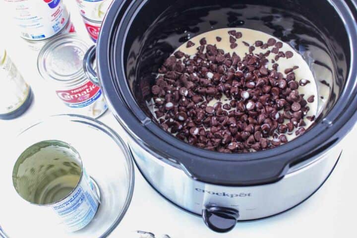 Evaporated milk poured into a slow cooker with chocolate chips for Mexican hot chocolate.