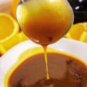 A metal spoon dipped in a bowl of thick, glossy orange teriyaki sauce.