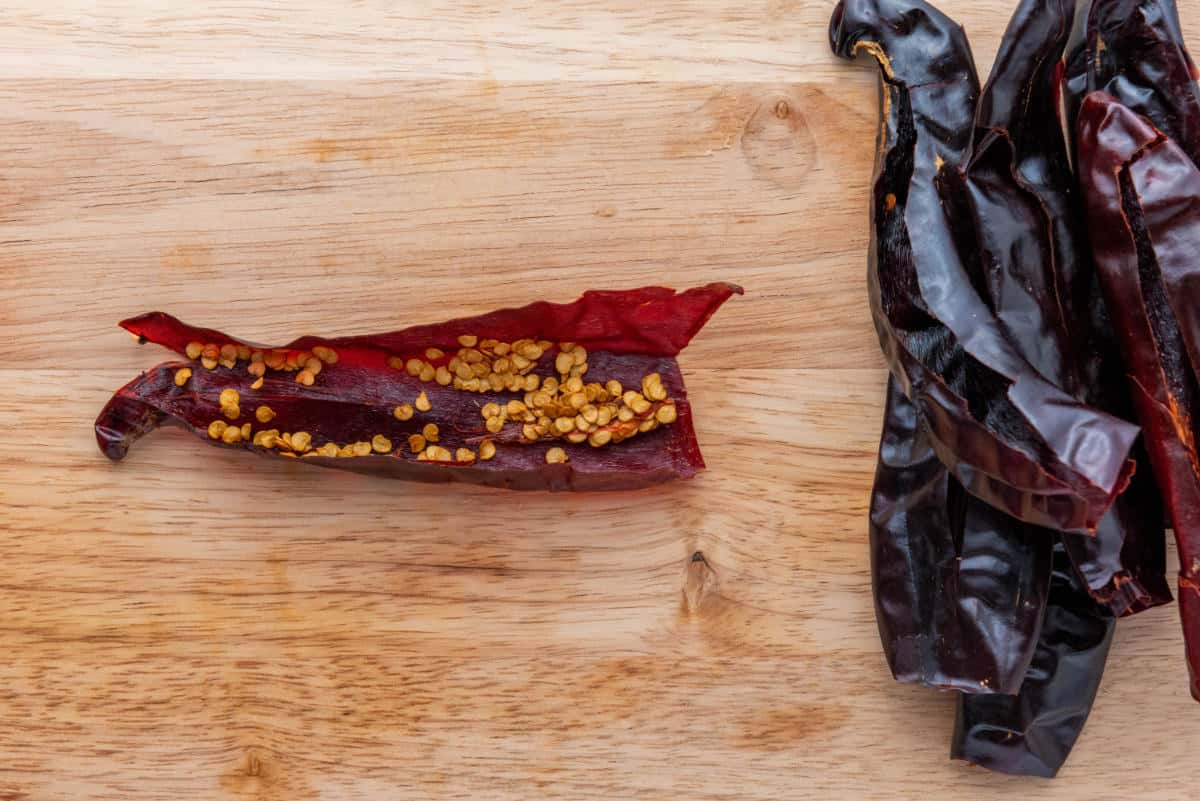 A dried guajillo chile split open with seeds removed on a wooden surface.