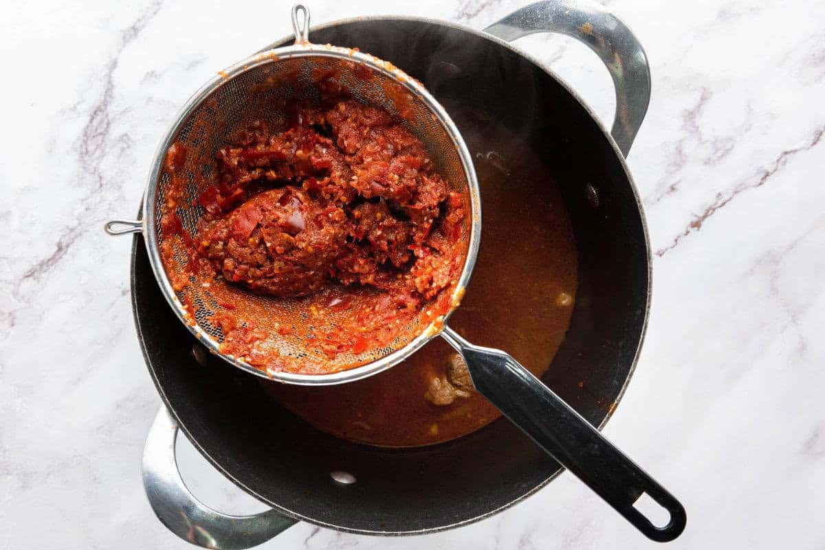 Blended chile sauce being strained into a pot of broth.