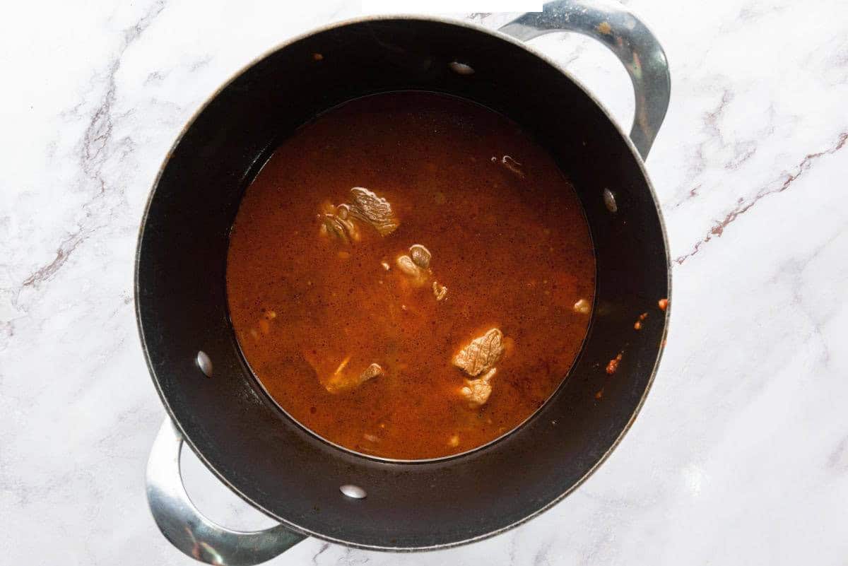 Birria stew with tender beef simmering in a rich red broth.