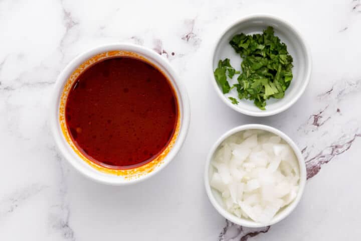 Bowls of consommé, chopped cilantro, and diced onions prepared for serving.