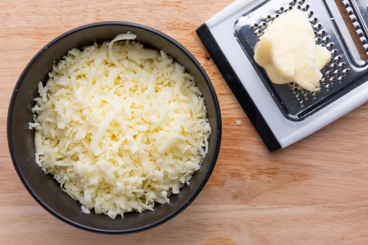 Shredded Oaxaca cheese in a bowl with a cheese grater.