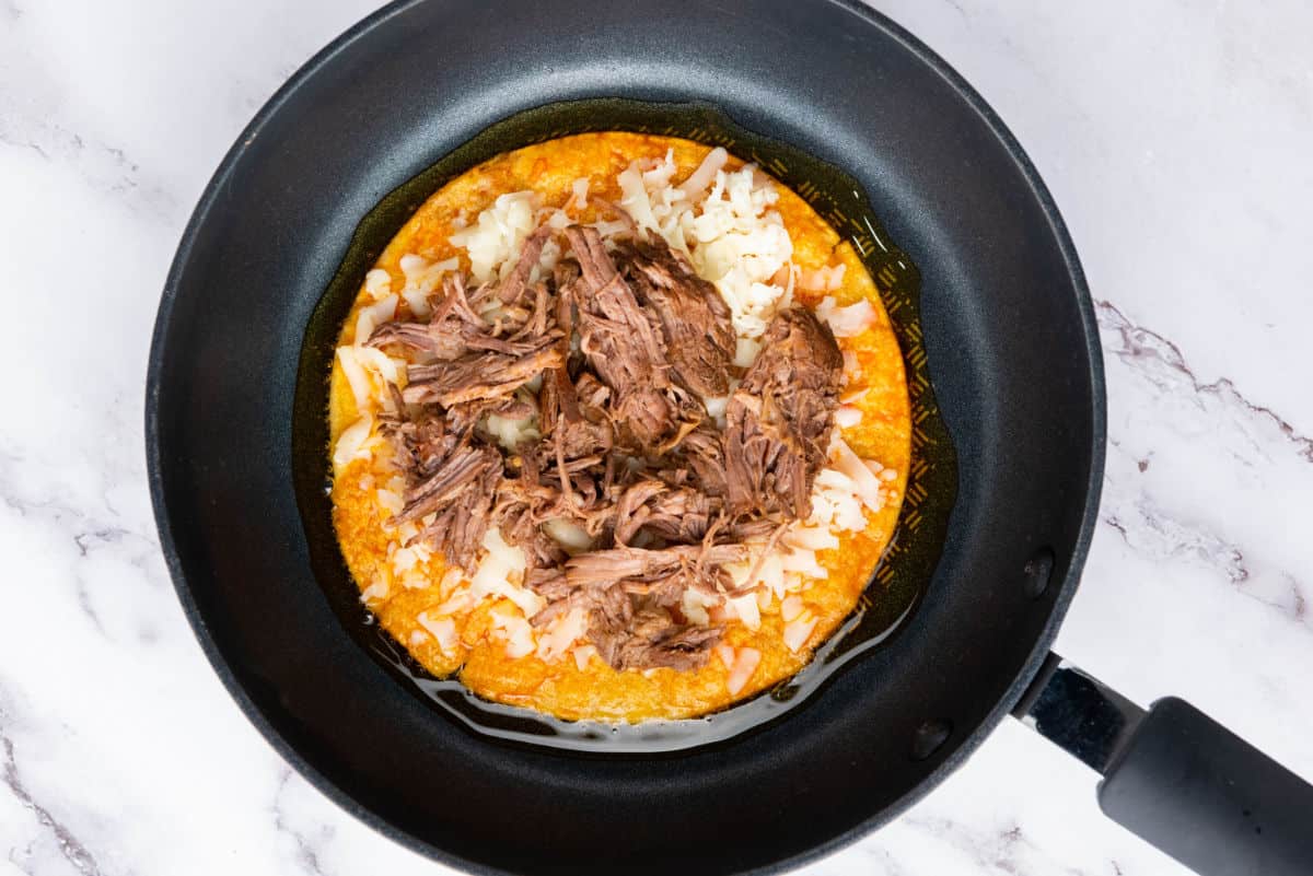 A taco cooking in a skillet with melted cheese and beef.