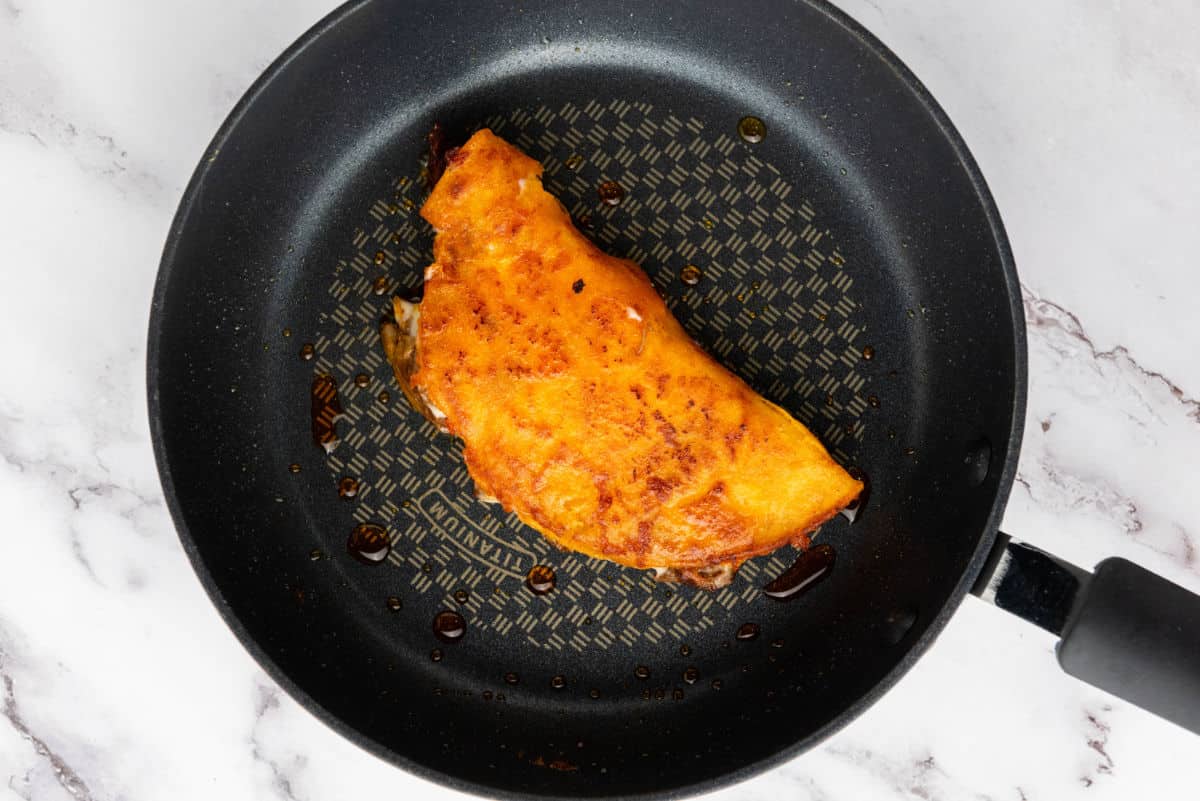 A folded quesabirria taco crisping in a skillet until golden.