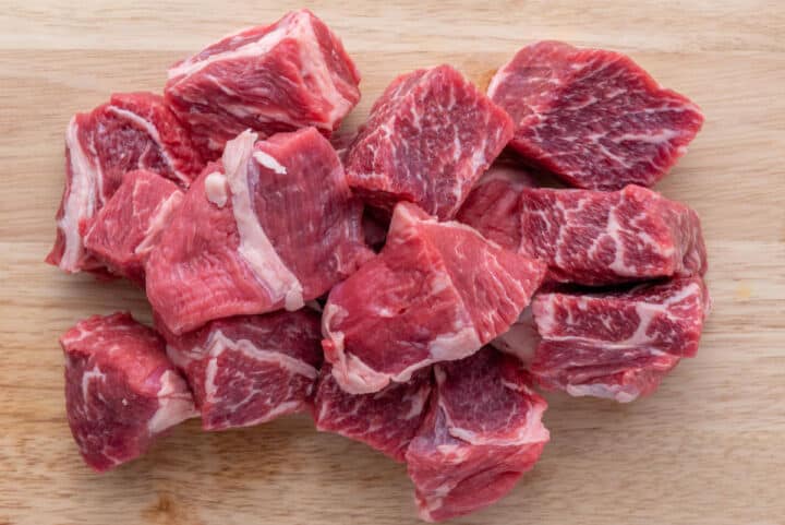 Raw beef chunks cut into large pieces on a wooden cutting board.