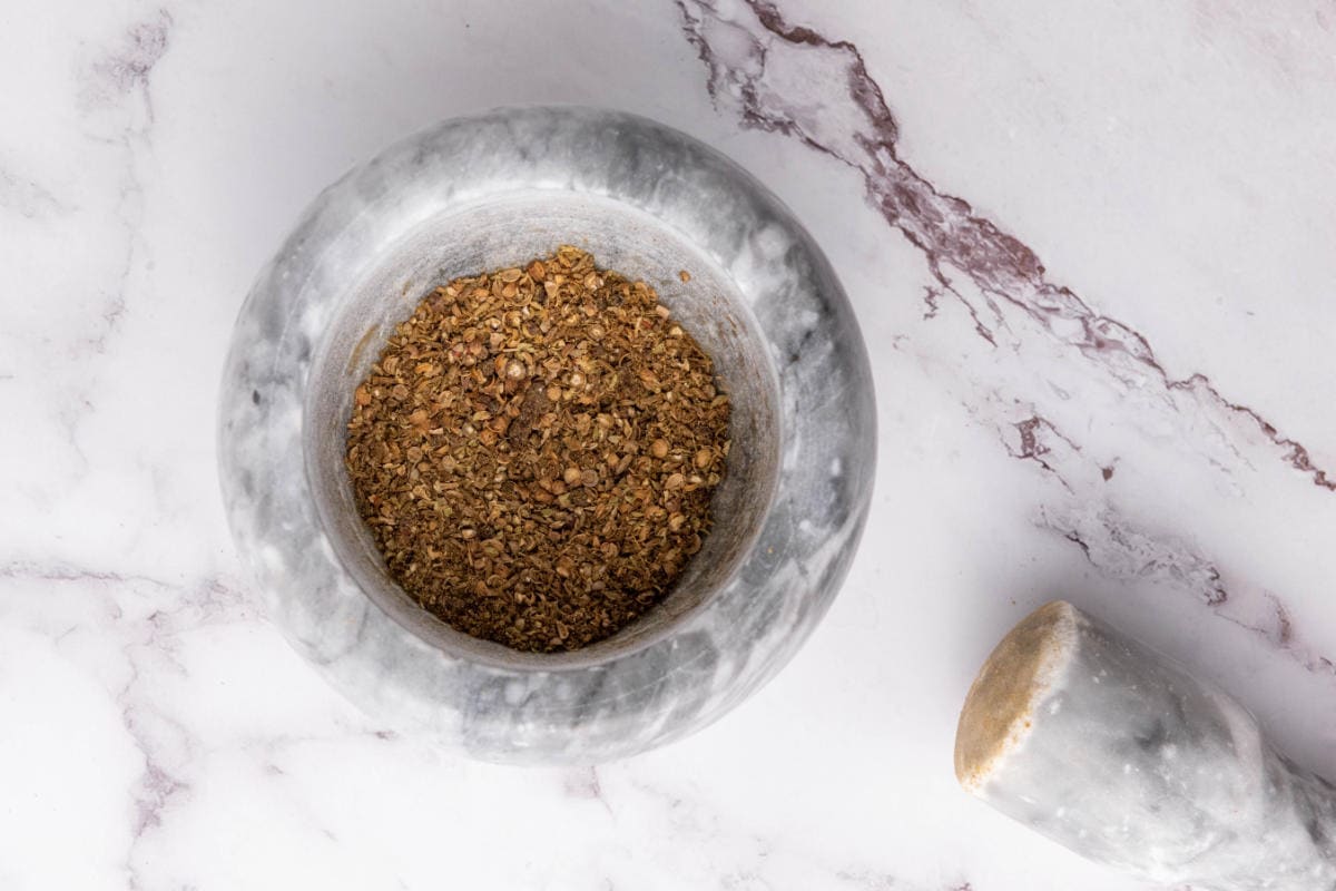 Ground spices in a mortar including cumin, coriander, peppercorns, and cloves.