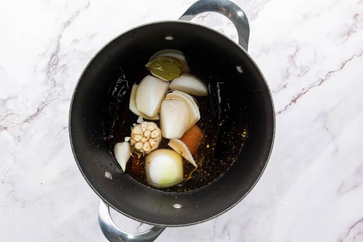 A pot filled with beef, onions, garlic, chiles, and broth before cooking.