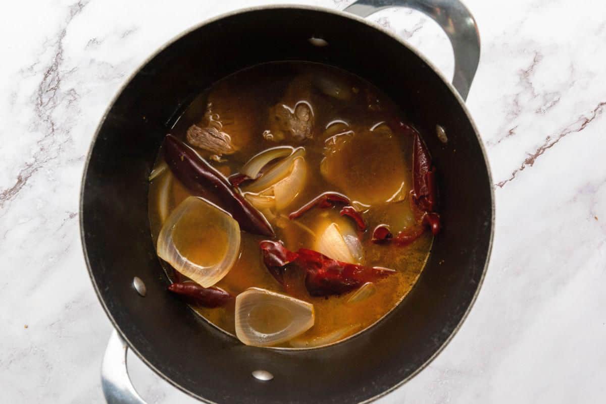 Beef simmering in broth with dried chiles and onions in a cooking pot.