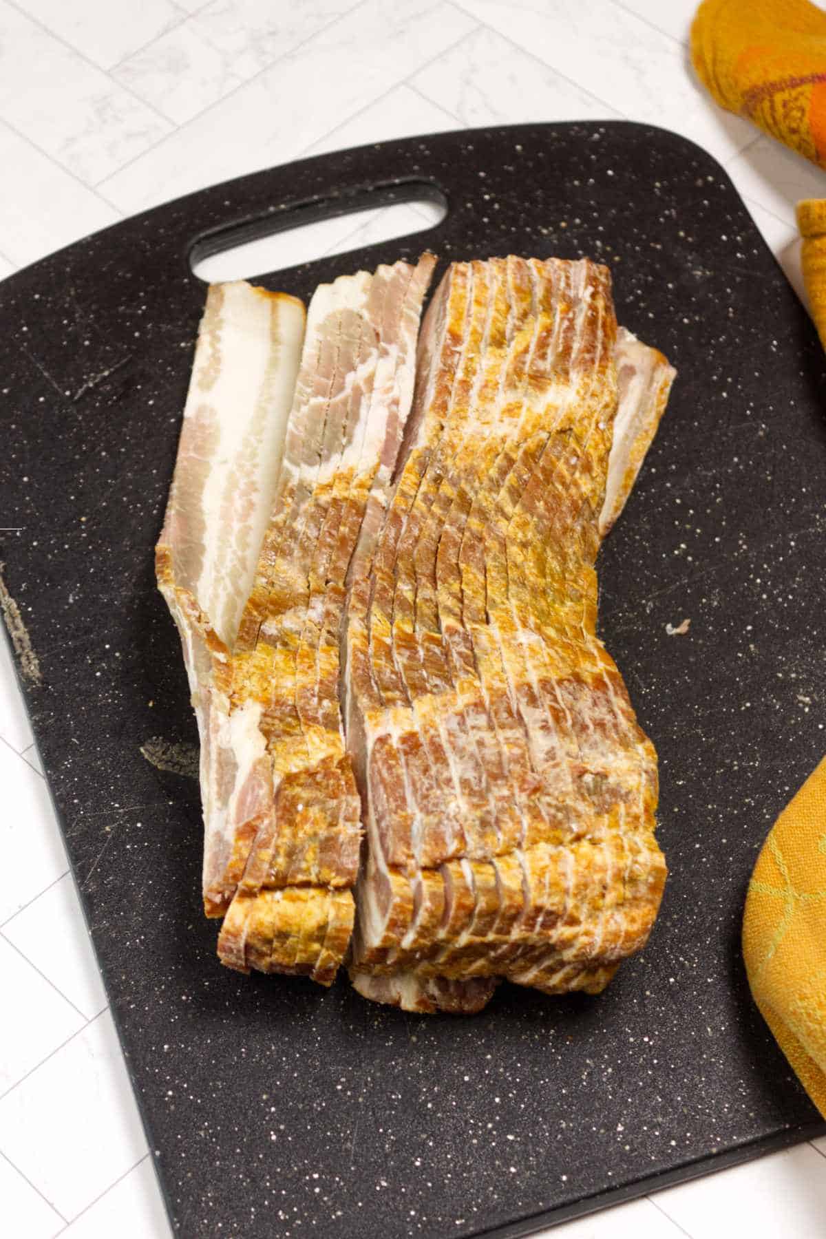 Raw bacon strips arranged on a cutting board ready for oven baking.