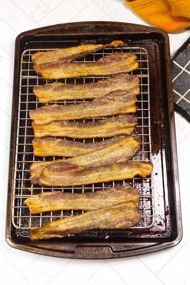 Fully cooked oven bacon resting on a rack over the sheet pan after baking.