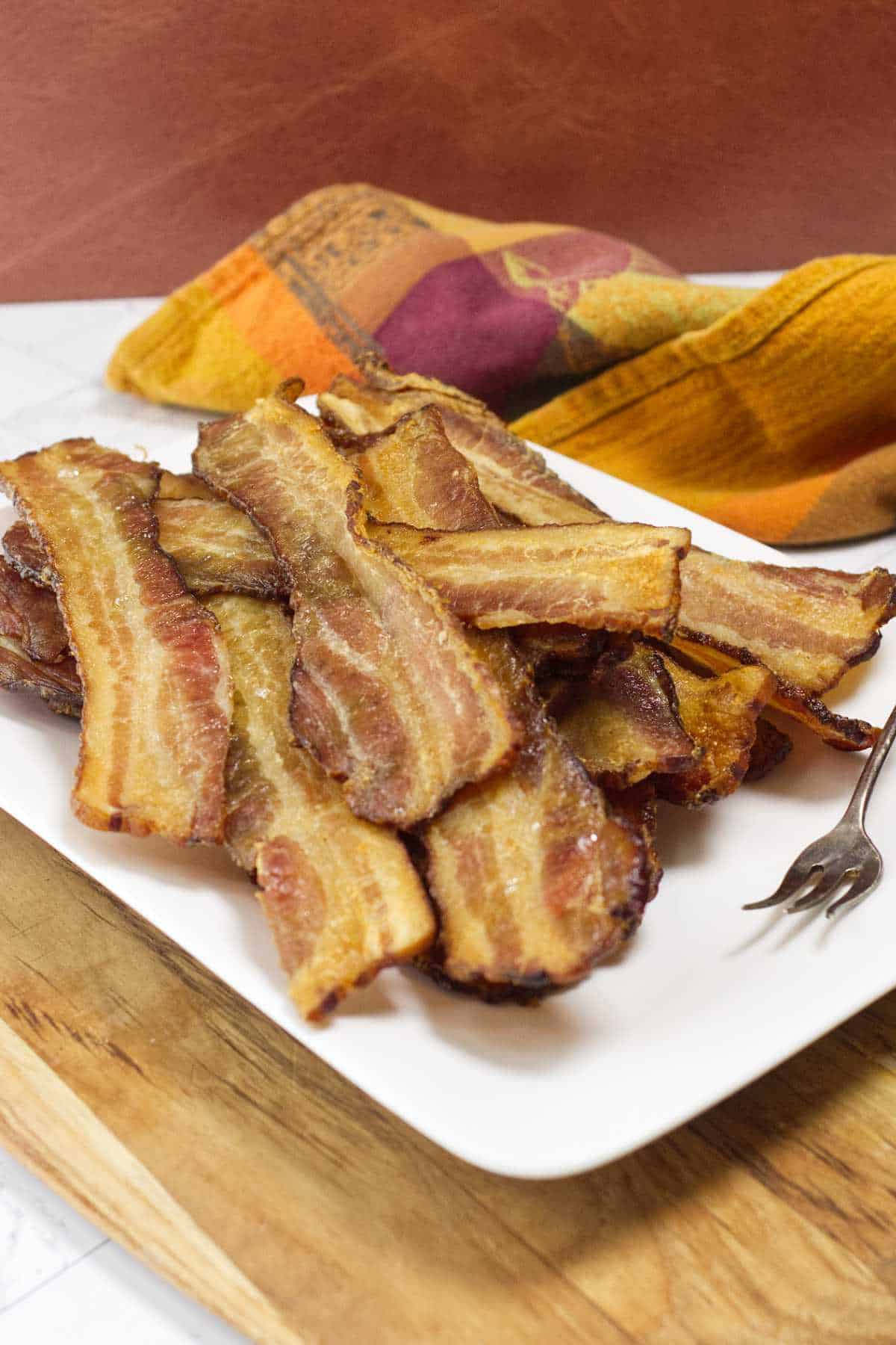 Crispy oven baked bacon served on a white plate on a wooden table.