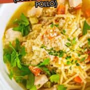 Bowl of chicken fideo soup with noodles, chicken, veggies, herbs, and grated cheese.