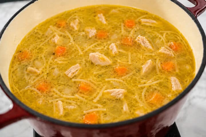 Mexican chicken fideo soup with thin noodles, chicken, carrots, and golden broth in a red Dutch oven.