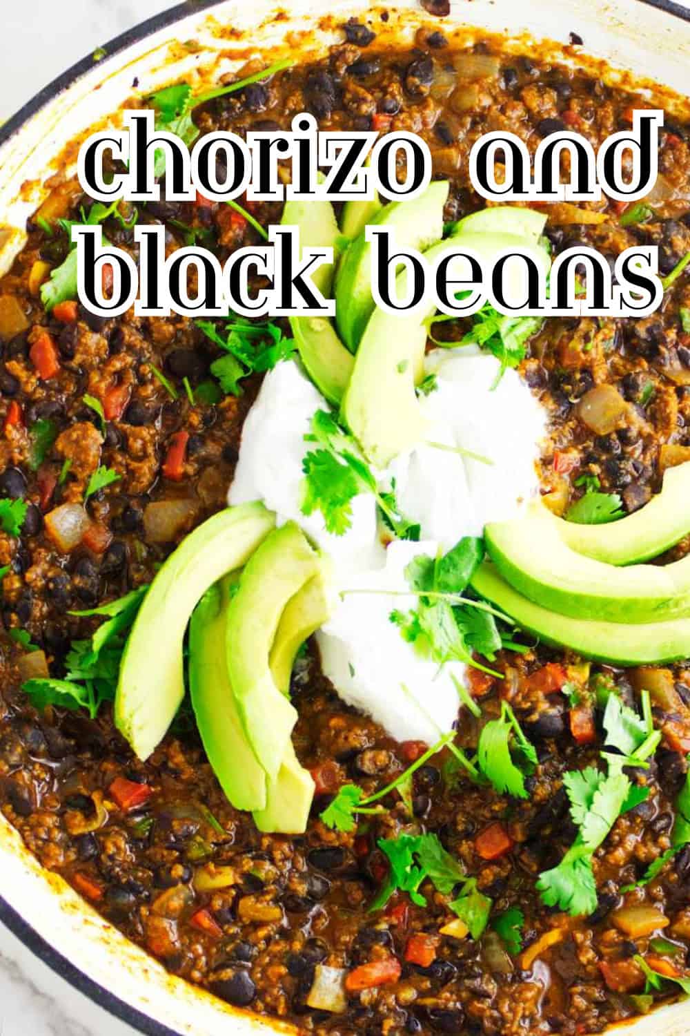 Chorizo and black beans topped with avocado, sour cream, and cilantro in a skillet.