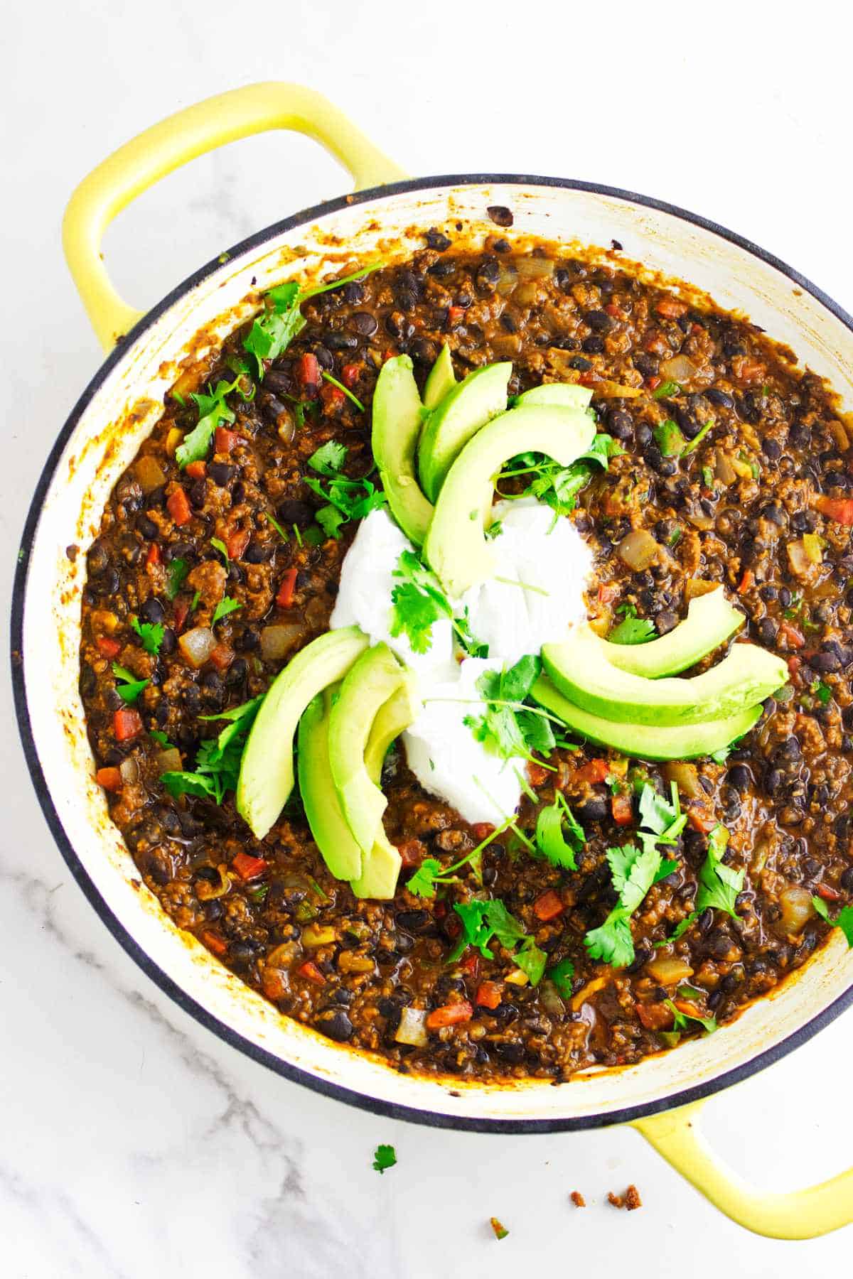 Skillet of chorizo refried beans garnished with avocado, sour cream, and cilantro.