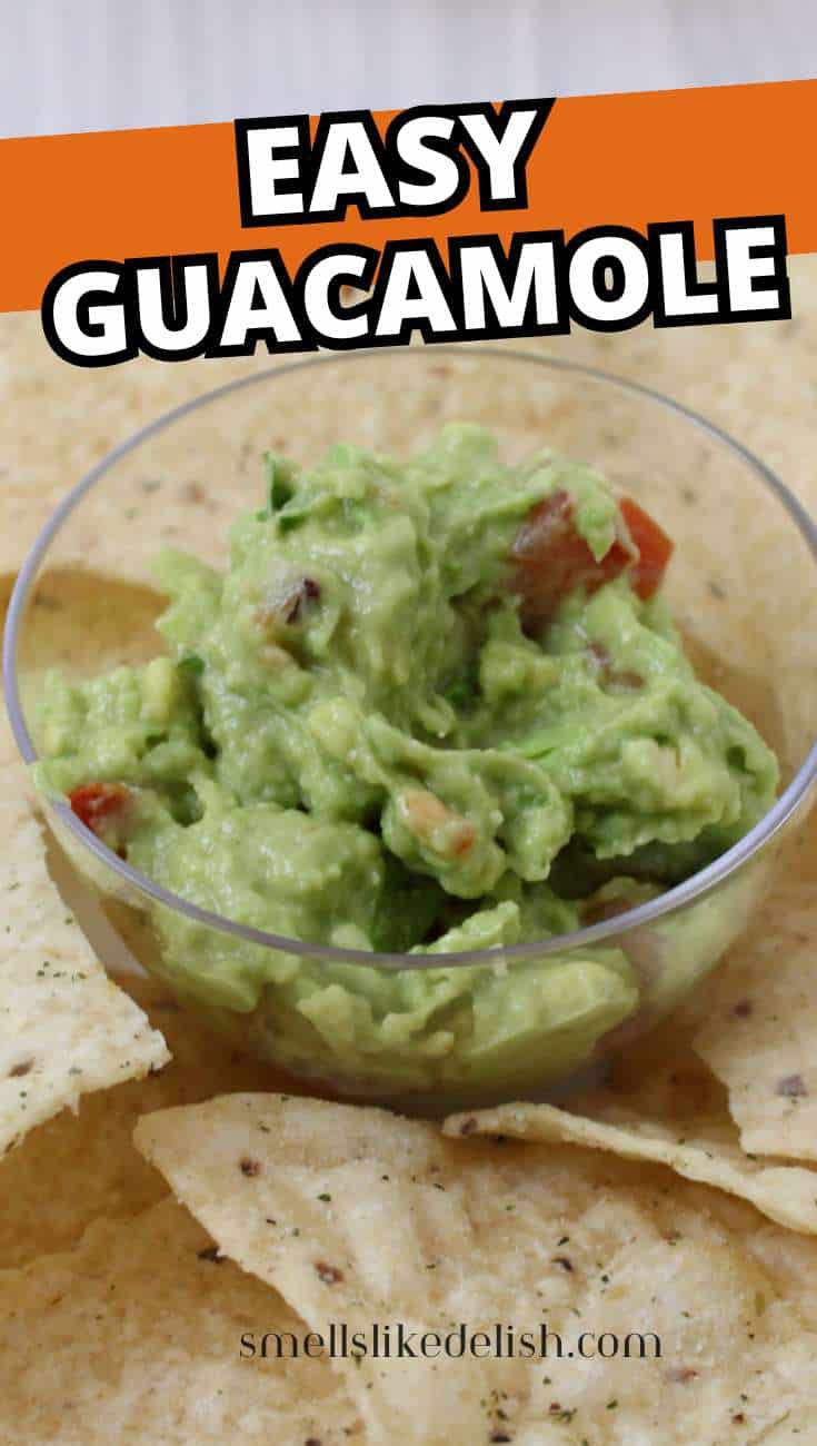 A clear bowl of guacamole with tomato pieces sits on a plate surrounded by tortilla chips.