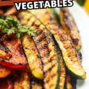 Close-up of charred zucchini and red bell peppers topped with herbs.