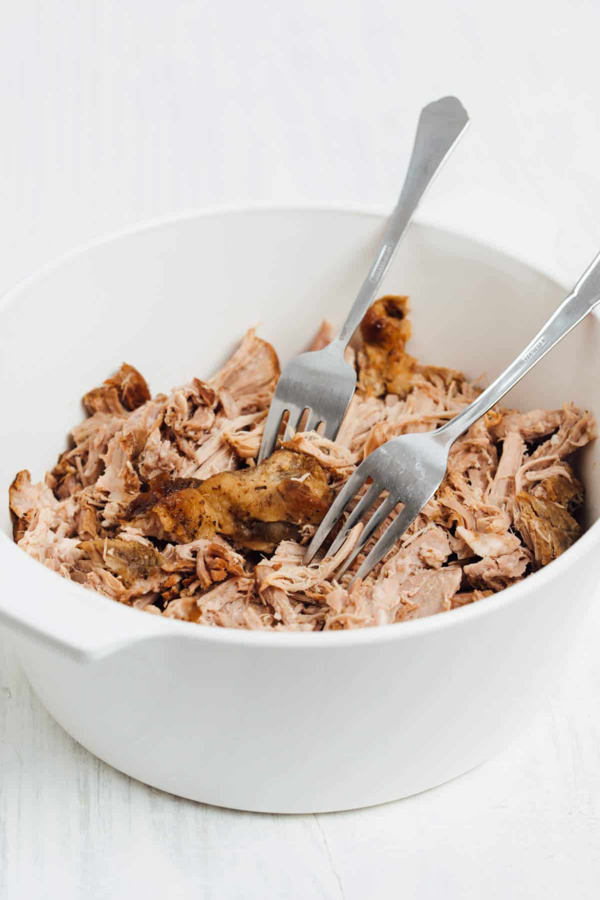 Two forks pull apart tender Instant Pot pork butt in a white bowl.
