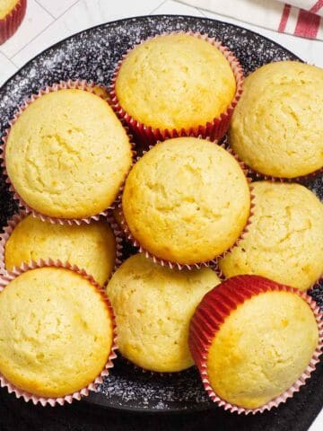 Mantecadas with orange zest in red liners on a black plate.