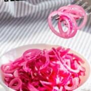 A white bowl filled with bright pink Mexican pickled onions sits on a counter, while a fork lifts several onion rings above the bowl.