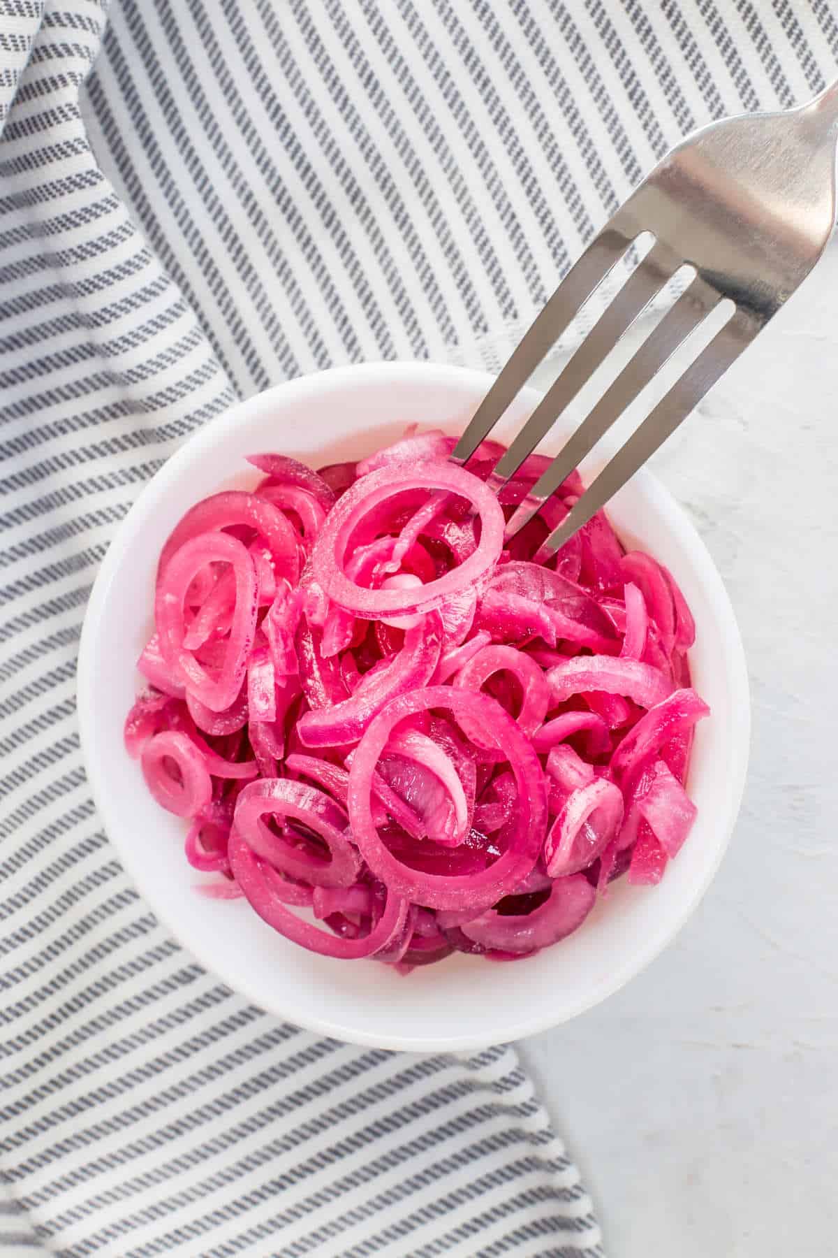 Bowl of Mexican pickled onions with a fork on a blue and white striped towel.