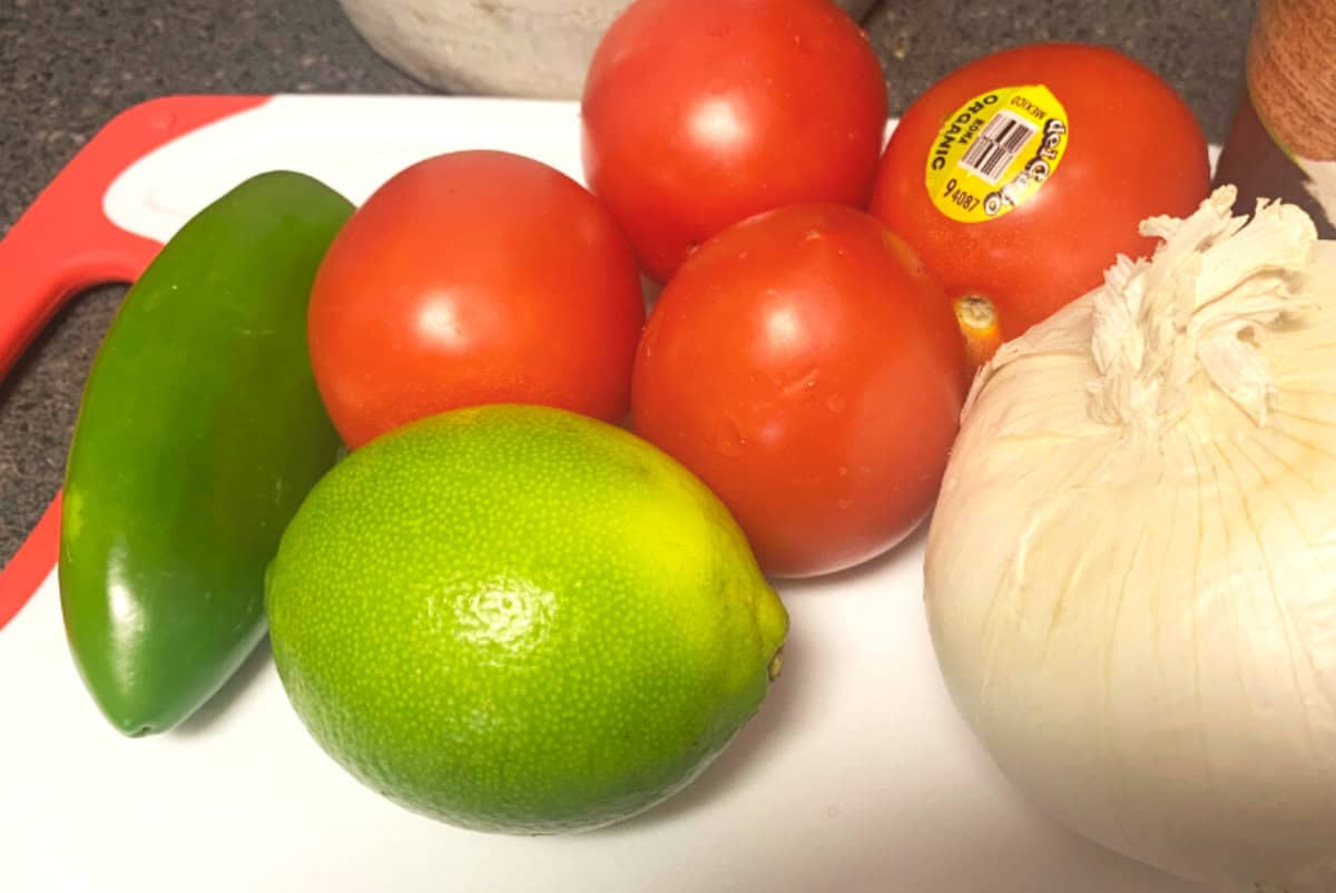 Ingredients for pico de gallo including tomatoes, onion, jalapeno, and lime on a cutting board.