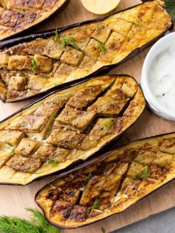 Roasted eggplant halves with garlic dill yogurt sauce, lemon, and fresh herbs.
