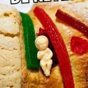 Rosca de Reyes topped with candied fruit and a plastic baby, shown close-up with "Rosca de Reyes" text at the top.