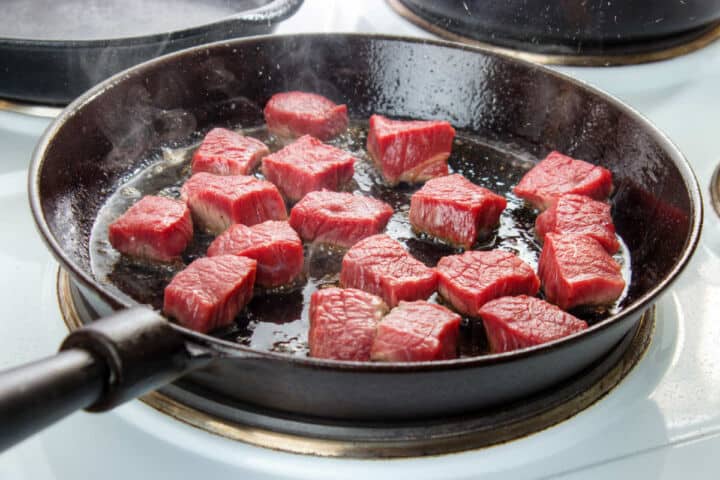 Seasoned steak pieces searing in a cast iron skillet for steak quesadillas.