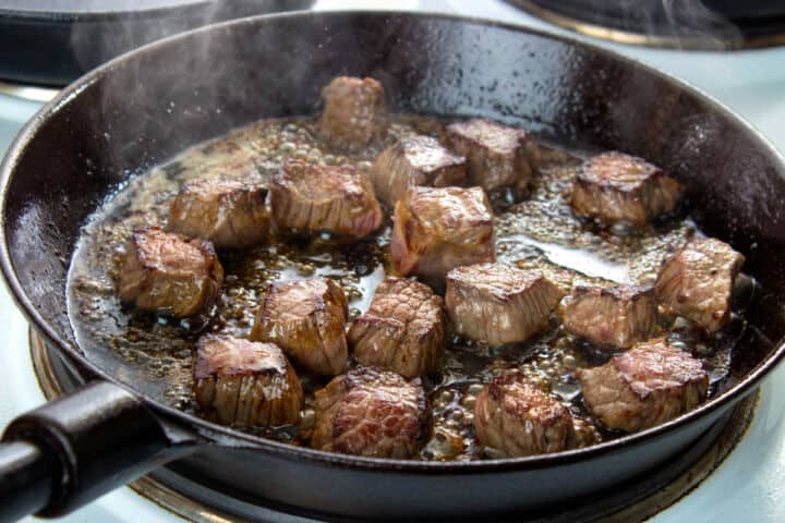 Steak pieces browning in a cast iron skillet for quesadillas.