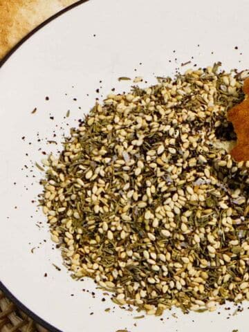 Pita bread dipped into homemade Za'atar seasoning with olive oil on a white plate.