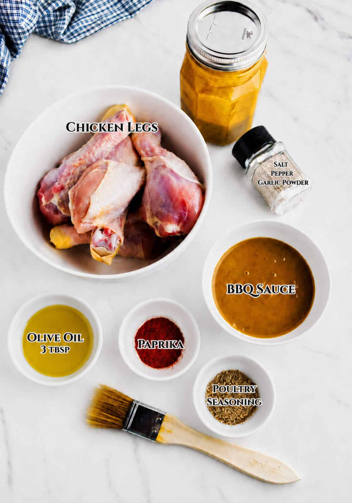 Ingredients for oven baked BBQ chicken drumsticks with chicken legs, BBQ sauce, olive oil, paprika, poultry seasoning, and seasonings.