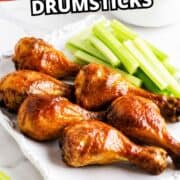 Glazed BBQ chicken drumsticks with celery on a white plate.