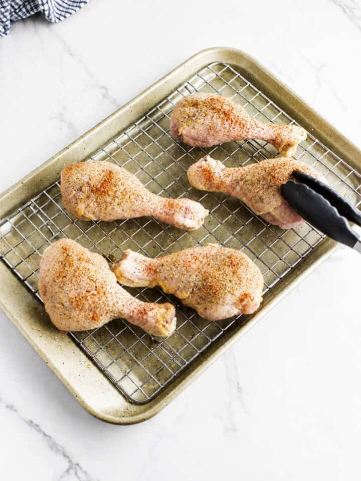 Seasoned chicken drumsticks arranged on a wire rack over a baking sheet before baking.