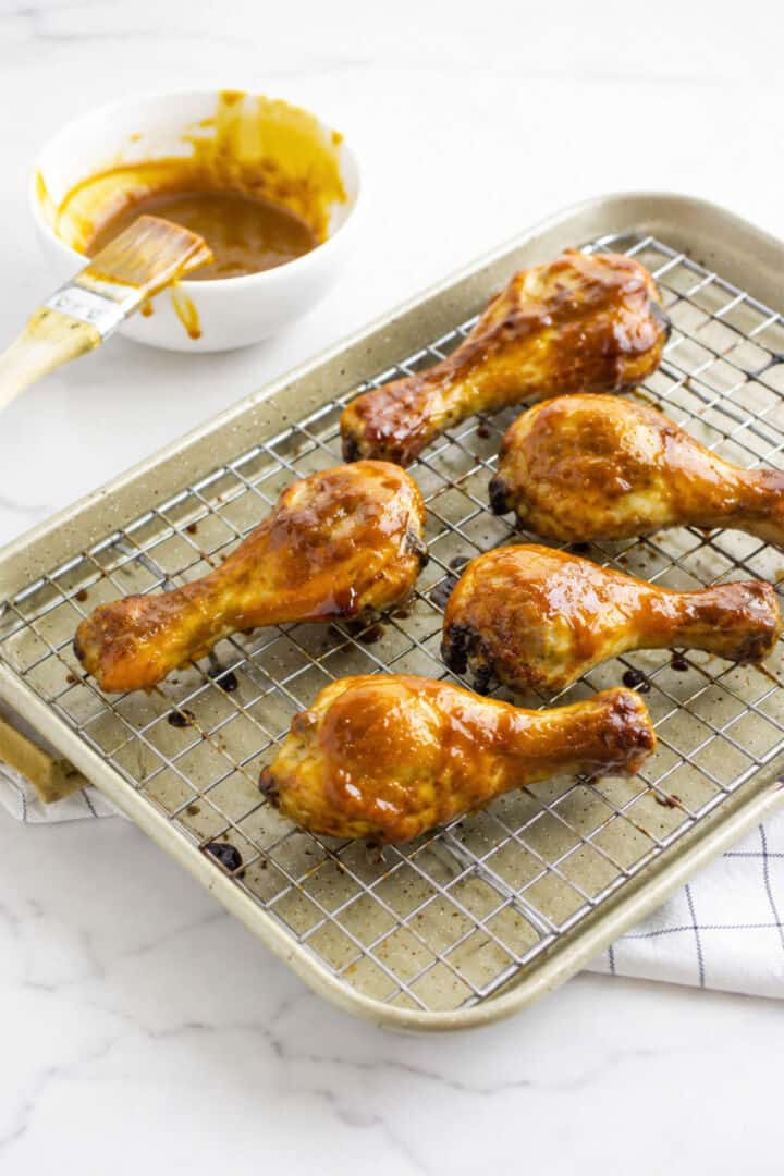 Glazed BBQ chicken drumsticks baking on a wire rack over a sheet pan.