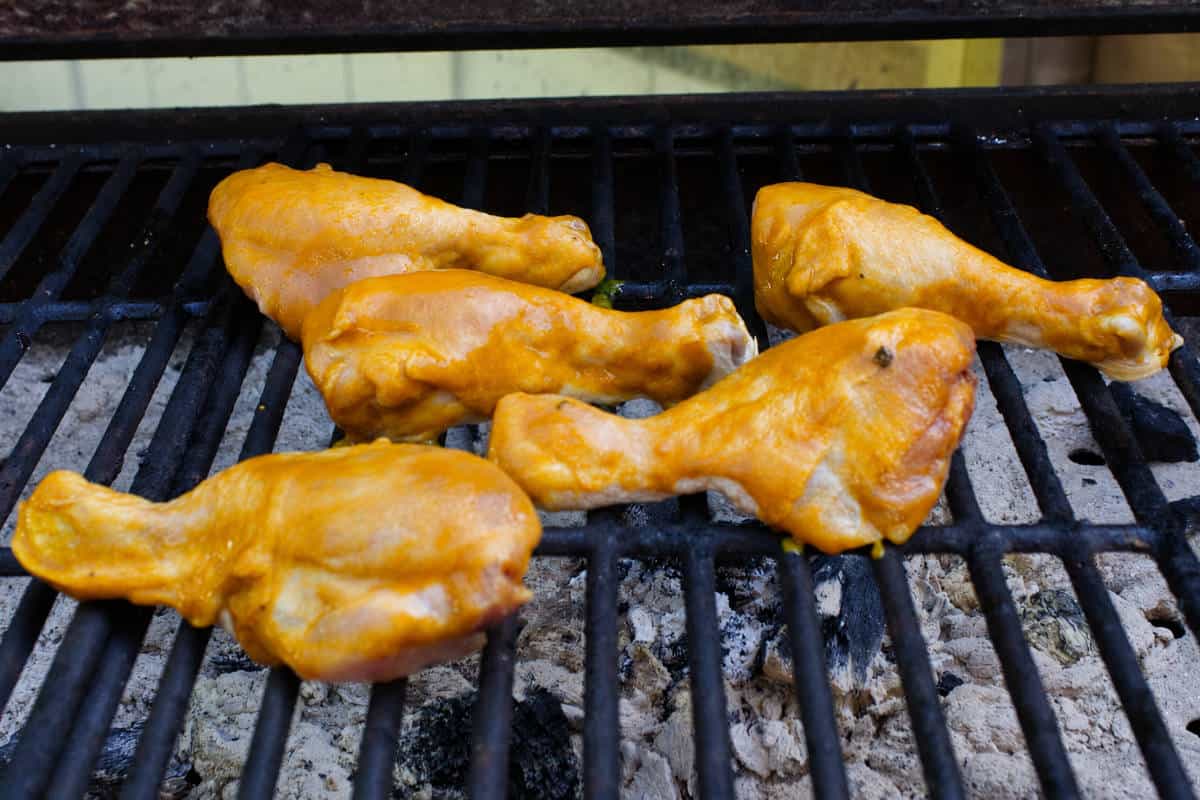 Chicken drumsticks cooking on an outdoor grill before being fully glazed with BBQ sauce.