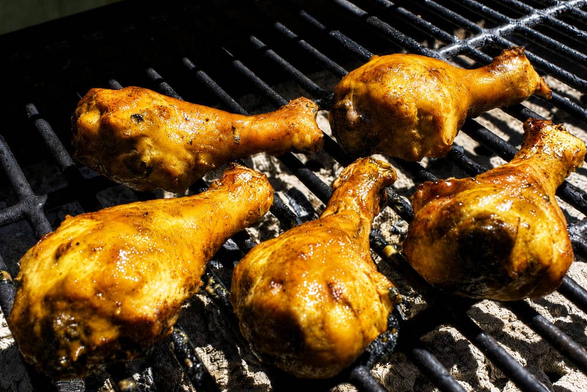 Grilled BBQ chicken drumsticks with caramelized sauce and light char marks on an outdoor grill.