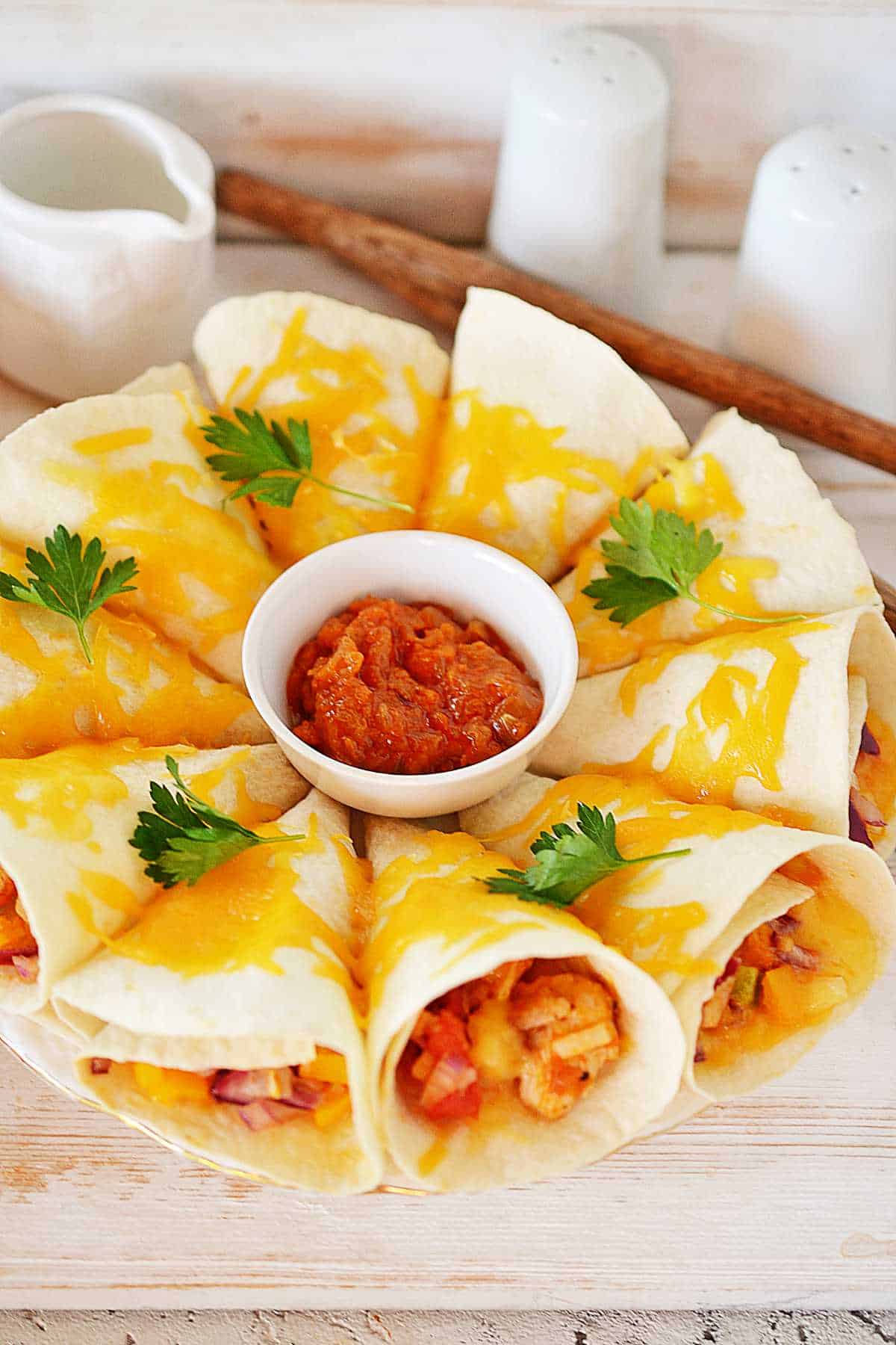 Tortilla cones with veggies and cheddar, arranged around salsa, garnished with parsley; salt and pepper shakers behind.