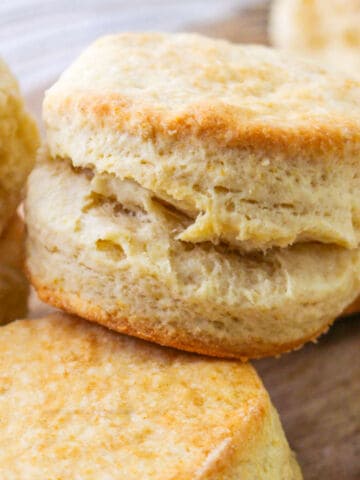 Golden, flaky biscuit with crisp top and visible layers on wooden surface among other biscuits.
