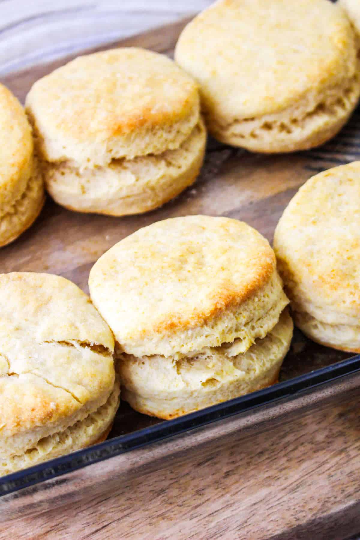 Golden, flaky biscuits with crisp tops and layers sit close together in a glass baking dish on a wooden surface.